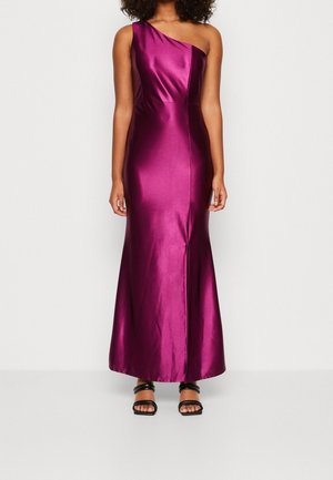 Femme portant une robe longue en satin magenta brillante avec une bretelle sur une épaule et des sandales à talons ouvertes noires.