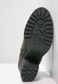 Suola in gomma nera con scanalature profonde e motivi a croce, abbinata a un superiore in camoscio grigio con dettagli di cucitura minimi.