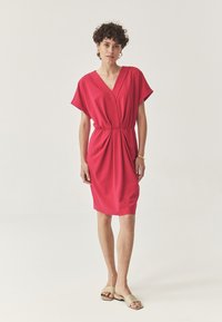 Rosa knielanges Kleid mit V-Ausschnitt, kurzen weiten Ärmeln und Raffung in der Taille. Weicher Stoff mit glatter Textur.