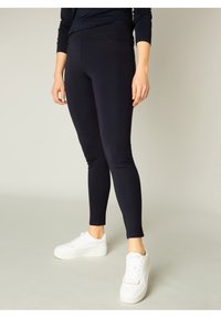Marineblauwe leggings van rekbaar materiaal, met een slim-fit ontwerp en enkellang, gecombineerd met witte sneakers.