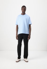 T-shirt en coton bleu clair à manches courtes, col rond et logo brodé. Associée à un pantalon noir et des baskets crème.