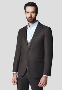 Brązowa marynarka garniturowa z dwoma guzikami, klapami w stylu notch oraz bocznymi kieszeniami. Nosi się ją na jasnoniebieskiej koszuli i szarym kamizelce. Gładka faktura.