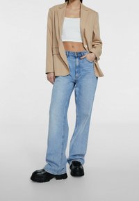Blazer beige a righe, top corto bianco, jeans a gamba larga in denim azzurro chiaro e scarpe platform nere chunky. Linee pulite e vestibilità casual.