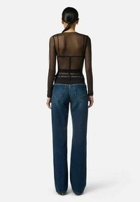 Top a maniche lunghe in rete nera con pannelli trasparenti e dettagli strutturati, abbinato a jeans in denim blu a vita alta con taglio dritto.