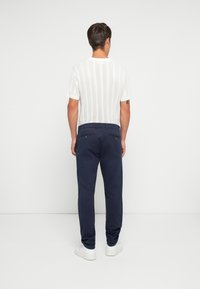 Maglietta bianca a maglia con maniche corte e chinos navy, caratterizzata da una vestibilità rilassata e tasche posteriori. Indossata con sneakers bianche.