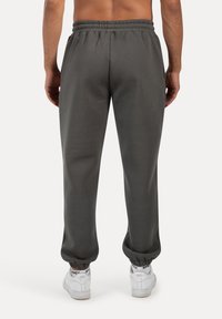 Grå sweatpants med elastisk talje og manchetter, der har en glat tekstur og en afslappet pasform, parret med hvide sneakers.