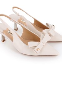 Tacones slingback de cuero beige con puntera afilada, acento de lazo, herrajes dorados y un tacón bajo. Textura suave y diseño elegante.