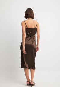 Vestido midi de satén marrón con tirantes delgados ajustables, una silueta entallada y una textura suave, que llega justo por debajo de la rodilla.