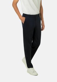 Marinefarbene Hose aus weichem Stoff mit geradem Bein, ausgestattet mit Seitentaschen und einem vorderen Knopfverschluss, kombiniert mit weißen Sneakers.