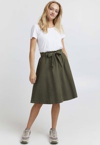 Olive green, knee-length skirt with a drawstring waistband and bow accent, paired with a white T-shirt and light-colored sneakers.