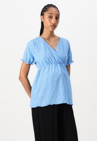 Hellblaue Bluse aus strukturiertem Stoff mit V-Ausschnitt, kurzen Rüschensäumen und Wickeldesign, das mit Lochstickereidetails versehen ist.