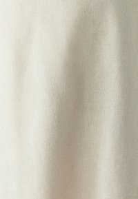 Světlý béžový textil s jemnou texturou a rovnoměrným tkaním, vykazující měkké záhyby a sklady, vhodný pro různé textilní aplikace.