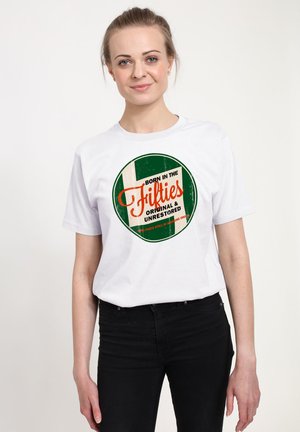 Ung kvinde iført hvid T-shirt med grønt og orange cirkeldesign med teksten "Born in the Fifties Original & Unrestored."
