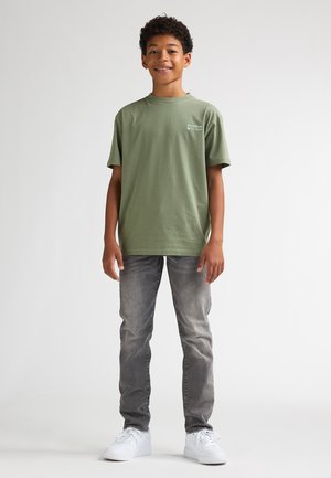 Olivengroen T-shirt met korte mouwen en een ronde hals, gecombineerd met grijze jeans en witte sneakers. Eenvoudig ontwerp, ongecomliceerde stof.