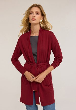 Cardigan lung burgundy din tricot moale, cu talie legată, buzunare frontale și accente ribbed pe mâneci pentru o textură suplimentară.