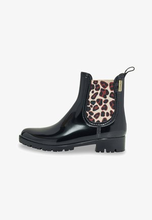 Bottines Chelsea noires étanches avec une finition brillante, présentant un panneau latéral élastique à imprimé léopard, une semelle en caoutchouc texturée et une languette.