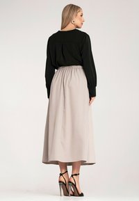 Czarna bluzka z długim rękawem, włożona w jasnobeżową maxi spódnicę z marszczonym pasem. Stylizację dopełniają czarne sandały na obcasie z paskami.