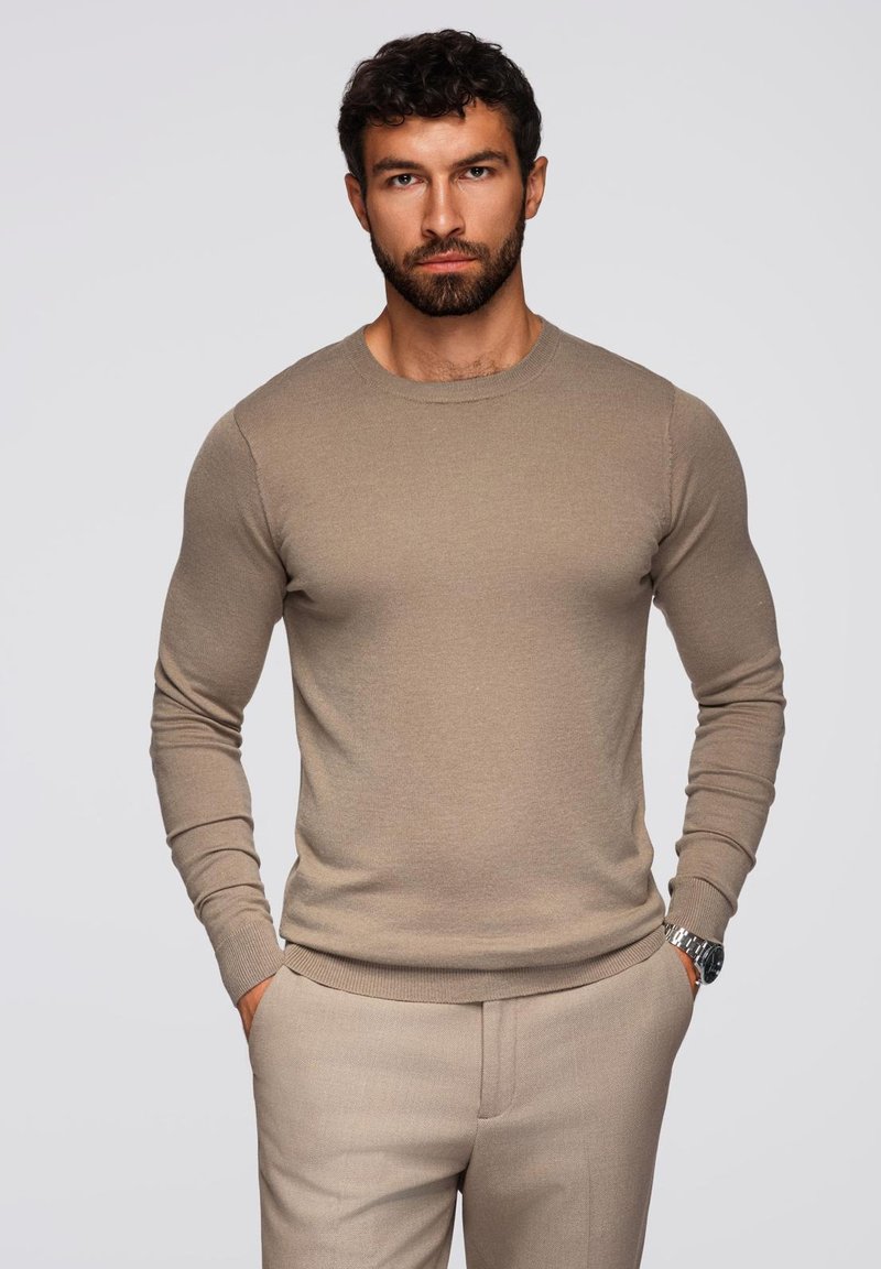 Beige crew-neck neule paita tiiviissä muotoilussa, valmistettu sileästä neulomateriaalista, yhdistettynä saman sävyisiin teksturoituihin beigeihin housuihin.