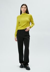 Maglione a coste giallo senape con collo alto, abbinato a pantaloni neri su misura e scarpe nere spesse con dettagli in catena.