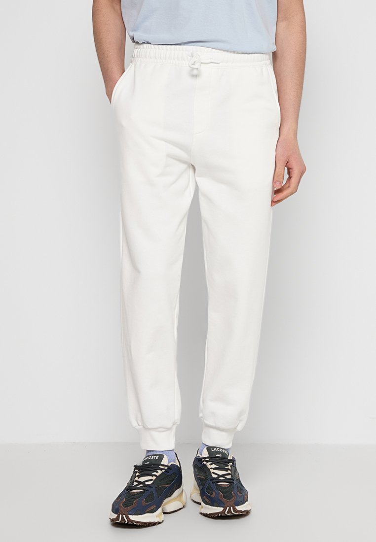 Witte sweatpants met een elastische tailleband, zijzakken en manchetten bij de enkels, gecombineerd met donkere sneakers met een patroon.