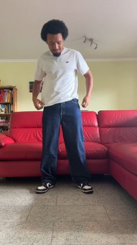 Μπλε τζιν παντελόνι, φαρδιά εφαρμογή, με ελαφριά φθορά και ορατές ραφές; συνδυασμένο με απλό λευκό μπλουζάκι και μαύρα-άσπρα αθλητικά παπούτσια.