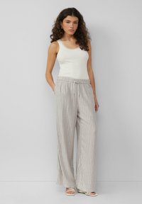 Lichte, grijs gestreepte wijde broek met een elastische tailleband en trekkoord. Gekleed met een aansluitend wit tanktop en sandaaltjes met banden.