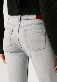 Ανοιχτό γκρι τζιν με εφαρμοστή σχεδίαση, με δύο πίσω τσέπες και διακριτικές ραφές. Η μέση έχει καφέ δερμάτινη ετικέτα.