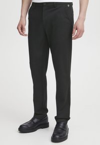 Schwarze maßgeschneiderte Hose aus glattem Stoff, mit geradem Bein, Gürtelschlaufen und praktischen seitlichen Taschen, kombiniert mit schwarzen Loafern.