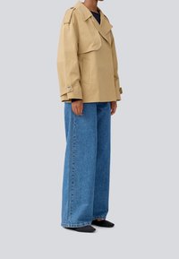 Beige cropped jakke med bred krave og store lommer, parret med løse, blå denimjeans. Mørke sko fuldender outfittet.