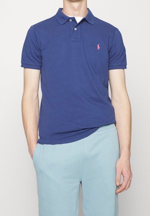 Marineblauw poloshirt van zachte katoen, met een klassieke kraag, korte mouwen en een klein roze geborduurd logo op de linkerborst.