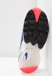 Semelle d'une chaussure de sport avec une bande de roulement noire, des accents rouges, un coussin d'air transparent et une partie supérieure bleue et blanche.