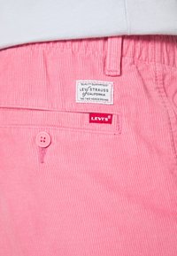 Pantalon en velours côtelé rose avec une poche boutonnée et des étiquettes de la marque Levi's cousues au-dessus de la poche et sur la couture.