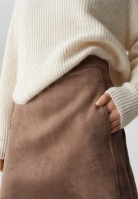 Beige gerippten Strickpullover über einem weichen braunen Wildledröck mit seitlichen Taschen, der eine glatte Textur und eine taillierte Passform zeigt.