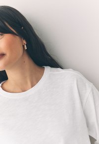 T-shirt bianca in cotone con scollo rotondo e vestibilità rilassata, caratterizzata da spalle leggermente scese e tessuto morbido e strutturato.