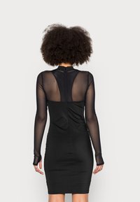 Czarna sukienka bodycon z długimi, przezroczystymi rękawami i transparentnym panelem z tyłu. Gładki materiał w dopasowanym kroju, wysoka szyja z zamkiem.