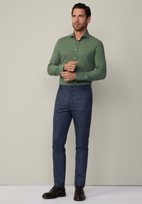 Groene button-up shirt met lange mouwen, gecombineerd met navy gekleurde slim-fit broeken met een patroon en donkere leren schoenen. Eenvoudig, op maat gemaakt ontwerp.