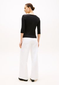 Crni top s tri četvrt rukavima uparен s bijelim širokim hlačama. Tkanina izgleda glatko; top ima izrez u obliku čamca i uski kroj.