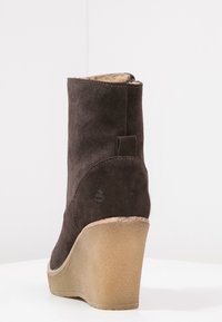 Brown suede wedge ankle boot with a textured upper and a curved, light-colored sole. Features a small heel accent at the back.
