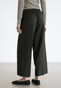 Schwarze, weit geschnittene Hose mit elastischem Bund, aus glattem Stoff und klaren Linien. Kombiniert mit schwarzen, slip-on Ballettschuhen.