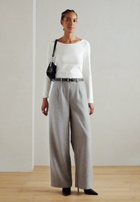White long-sleeve top paired with gray wide-leg trousers. Accessorized with a black handbag and a narrow belt, set against a neutral backdrop.