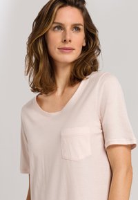 Ljusrosa t-shirt med kort ärm i mjukt material, med rund halsringning och en liten bröstficka, samt en slät yta.