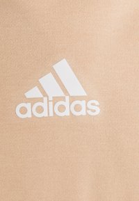 Tissu pêche clair avec un grand logo Adidas blanc. La texture est lisse avec un motif tricot subtil.