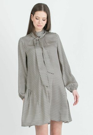 Schwarz-weißer gemusterter Kleid mit hohem Kragen und Schleifendetail, langen Ärmeln und ausgestelltem Saum; aus leichtem Stoff gefertigt.