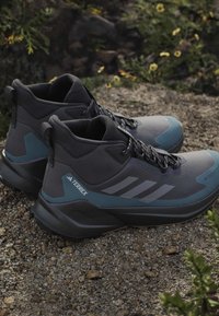 Botas de senderismo de caña alta en negro y azul con material sintético texturizado, puntera reforzada y branding de tres rayas en gris.