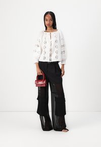 Weiße bestickte Bluse mit Puffärmeln, schwarze durchsichtige weite Hose und eine kleine rote Handtasche mit Oberringen. Minimalistisches Design.