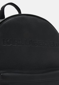 Fekete bőrtáska textúrált felülettel, kerek tetejével és a "KARL LAGERFELD" logóval a frontrészen. Simaságot sugalló pántokkal.