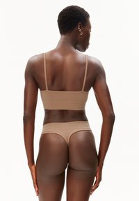 Beige naadloze bh en string set met dunne bandjes en een gladde textuur, met een minimalistisch ontwerp. Achteraanzicht benadrukt de pasvorm en eenvoud.