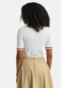 Top blanco de manga corta con canalé y puños a rayas en naranja, azul marino y blanco, combinado con una falda beige de cintura alta que presenta un detalle de cremallera.