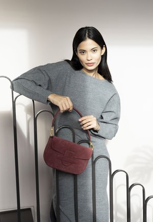 Red suede handbag with a structured design and subtle embossed detail, featuring a short handle and gold hardware accents.