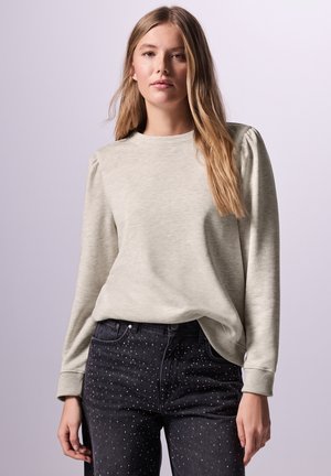 Lichtgrijze sweatshirt met een ronde hals, geribbelde manchetten en licht poffende mouwen. gecombineerd met zwarte spijkerbroek met zilveren studs.